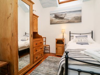 A bedroom with a single bed a wooden wardrobe with a mirror a wooden chair a wooden chest of drawers a small wooden bedside table with a lamp and a painting of a boat on the wall at The Shippen in Gooseham near Kilkhampton