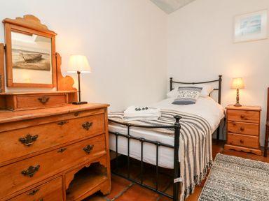 A bedroom with a single bed iron frame wooden dresser with mirror and a bedside table with lamps at The Shippen in Gooseham near Kilkhampton