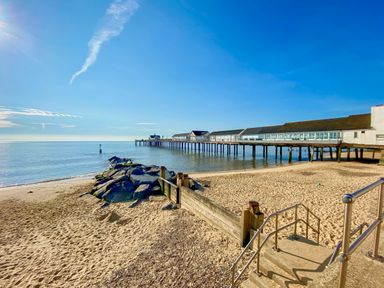A sandy beach with rocks and a wooden barrier next to a pier extending into the sea at Sea Mouse Cottage in Southwold
