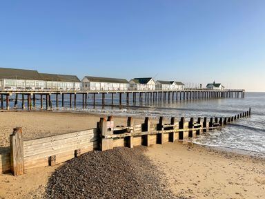 A sandy beach with wooden groynes and a long pier with buildings over the water at Sea Mouse Cottage in Southwold