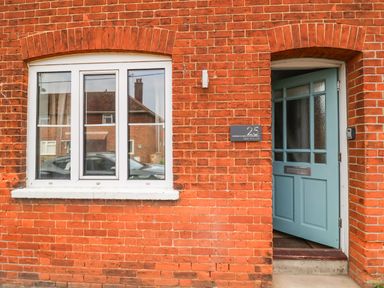 A brick exterior wall with a white framed window and a partially open blue door at Sea Mouse Cottage in Southwold