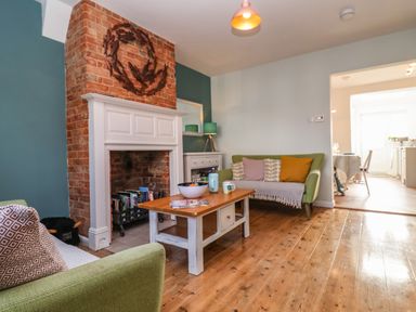 A living room with a brick fireplace a wooden coffee table two green sofas and a lamp at Sea Mouse Cottage in Southwold