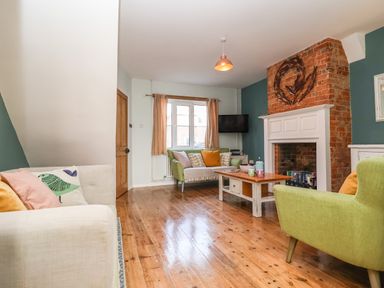 A living room with wooden floor a brick fireplace two green armchairs a beige sofa and a wooden coffee table at Sea Mouse Cottage in Southwold