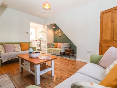 A living room with two green sofas a wooden coffee table and a small seating area under stairs at Sea Mouse Cottage Southwold