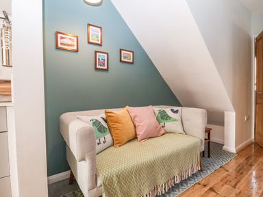 A small seating area with a beige sofa and colorful cushions under a slanted ceiling at Sea Mouse Cottage in Southwold