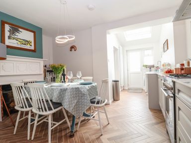 A dining area with a table set for four chairs a kitchen with appliances and a door leading outside at Sea Mouse Cottage Southwold