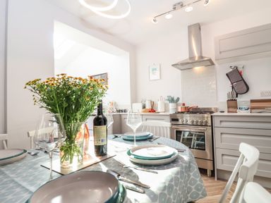 A kitchen with a dining table set with plates glasses and a vase of flowers at Sea Mouse Cottage in Southwold