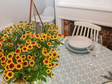 A dining table with plates glasses and a bouquet of yellow and red flowers at Sea Mouse Cottage in Southwold