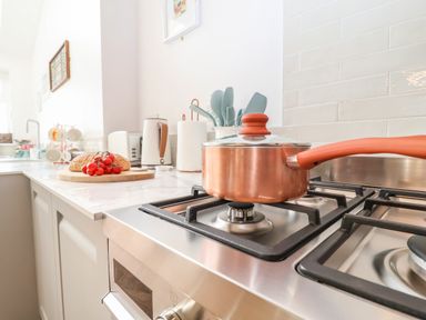 A kitchen countertop with a copper saucepan on a gas stove and bread with tomatoes on a cutting board at Sea Mouse Cottage in Southwold