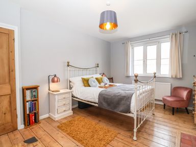 A bedroom with a white metal bed frame two bedside tables with lamps a pink chair and a small bookshelf at Sea Mouse Cottage Southwold