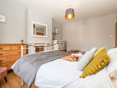A bedroom with a bed and breakfast tray next to a wooden dresser and a mirror above a fireplace at Sea Mouse Cottage Southwold