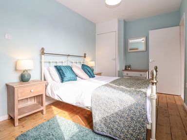 A bedroom with a bed pillows side tables lamps a blue rug and wooden floor at Sea Mouse Cottage in Southwold