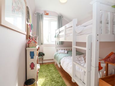 A small bedroom with a white bunk bed green rug and a window at Sea Mouse Cottage in Southwold