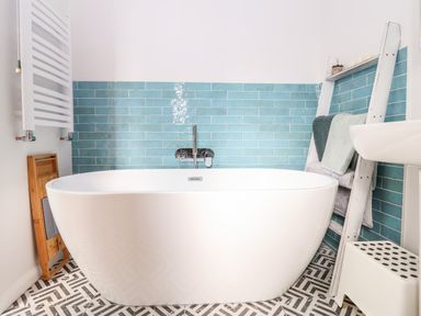 A bathroom with a freestanding white bathtub blue subway tiles white towel ladder and patterned floor tiles at Sea Mouse Cottage in Southwold