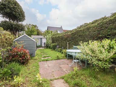 A garden with a green shed a paved seating area with a bench and table and a hedge at Sea Mouse Cottage in Southwold