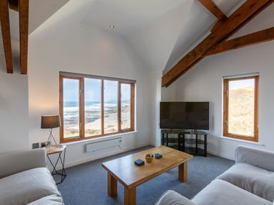 A living room with two sofas a wooden coffee table a television and windows showing a beach view at Sunset View in Widemouth Bay