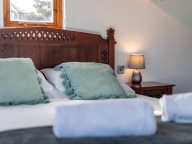 A bed with green pillows and a bedside table with a lamp in a bedroom at Sunset View in Widemouth Bay