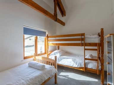 A bedroom with wooden bunk beds and a single bed under a window at Sunset View in Widemouth Bay