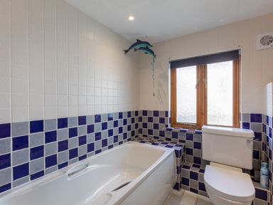 A bathroom with a bathtub a toilet and a window with blue and light blue tiled walls at Sunset View in Widemouth Bay