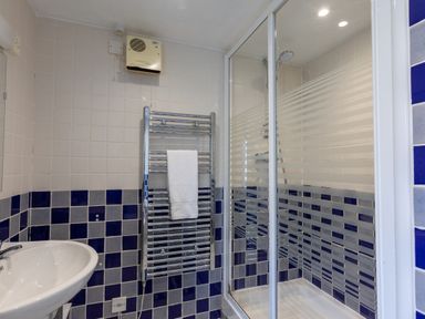 A bathroom with a shower enclosure a towel rack with a white towel and a sink at Sunset View in Widemouth Bay