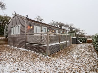 A wooden cabin with a fenced deck and snow on the ground at Grouse Lodge in Seamer North Yorkshire