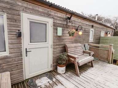 An outdoor wooden deck with a bench plant pots hanging basket and a white door at Grouse Lodge in Seamer North Yorkshire
