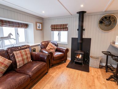 A living room with leather sofa and armchair near a wood burning stove and large wall clock at Grouse Lodge Seamer North Yorkshire