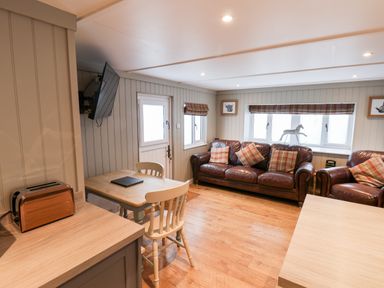 A living area with brown leather sofas plaid cushions wooden dining table white chairs and mounted TV at Grouse Lodge in Seamer North Yorkshire