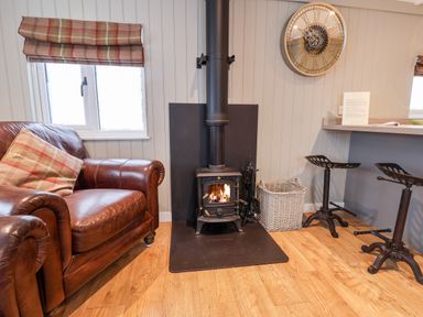 A room with a leather armchair a wood-burning stove and two metal bar stools at Grouse Lodge in Seamer North Yorkshire