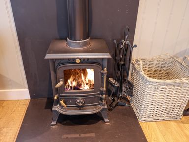 A wood burning stove with fire burning inside a room next to a wicker basket and fire tools at Grouse Lodge in Seamer North Yorkshire