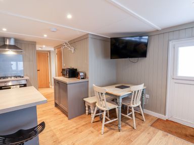 A kitchen area with a dining table two chairs a wall mounted TV and wooden doors at Grouse Lodge in Seamer North Yorkshire