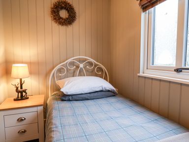 A bedroom with a bed with plaid bedding a bedside table with a lamp and a window at Grouse Lodge Seamer North Yorkshire
