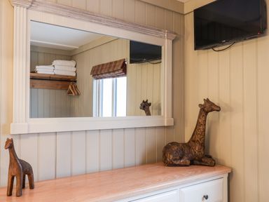 A room with a wall-mounted mirror reflecting a shelf with towels and hangers two giraffe sculptures on a wooden countertop and a wall-mounted TV at Grouse Lodge in Seamer North Yorkshire