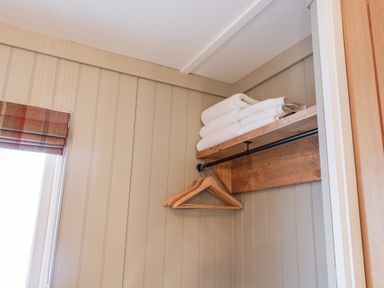 A wall with vertical paneling a window with a plaid blind a wooden shelf holding folded white towels and wooden hangers on a hanging rod at Grouse Lodge in Seamer North Yorkshire