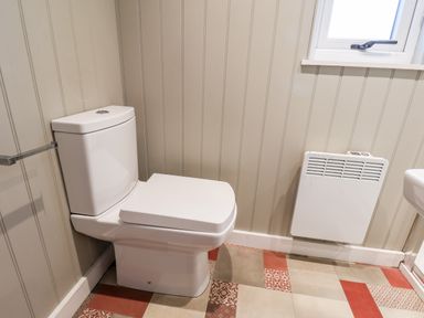 A bathroom with a white toilet a wall-mounted heater a window and patterned floor tiles at Grouse Lodge in Seamer North Yorkshire