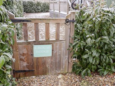 A wooden gate with a sign saying Grouse Lodge surrounded by frosted green bushes and gravel at Grouse Lodge in Seamer North Yorkshire