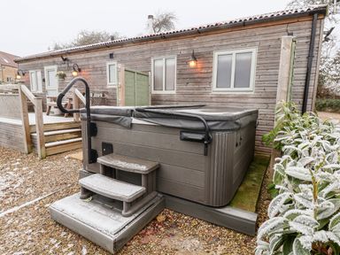 An outdoor hot tub with steps and handrails next to a wooden building with windows and lights at Grouse Lodge in Seamer North Yorkshire