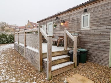 A wooden porch with stairs outside a building with two trash bins on gravel at Grouse Lodge in Seamer North Yorkshire