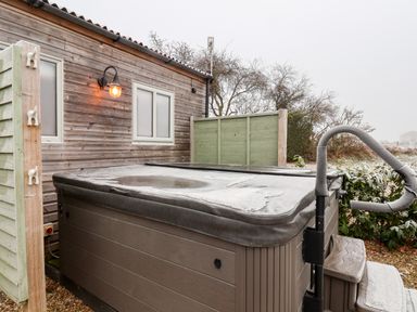 An outdoor hot tub with a cover next to a wooden building with a light and windows at Grouse Lodge Seamer North Yorkshire