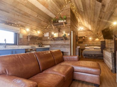A wooden room with a brown leather sofa blue kitchen cabinets and a bed at Foxes Den in Seamer North Yorkshire