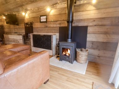 A living room with a wood burning stove leather sofa wooden walls and a basket of firewood at Foxes Den in Seamer North Yorkshire