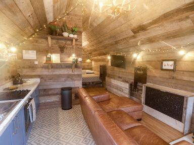 A living space with wooden walls a leather sofa a small kitchen and a bed at Foxes Den in Seamer North Yorkshire