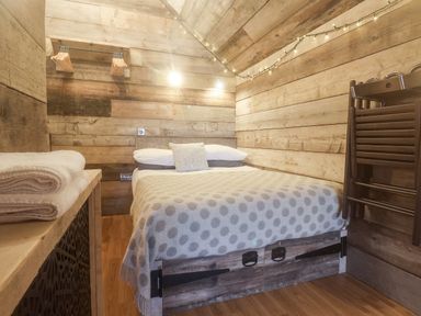 A small bedroom with a double bed wooden walls hanging lights and stacked wooden chairs at Foxes Den in Seamer North Yorkshire