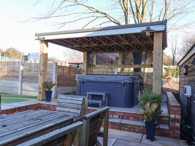 An outdoor patio area with wooden furniture a covered hot tub and potted plants at Foxes Den in Seamer North Yorkshire