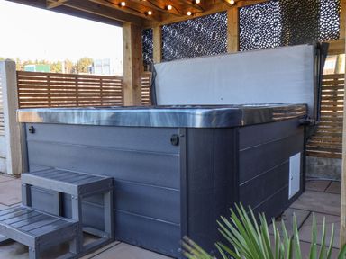 An outdoor hot tub with steps under a wooden pergola with decorative panels at Foxes Den in Seamer North Yorkshire