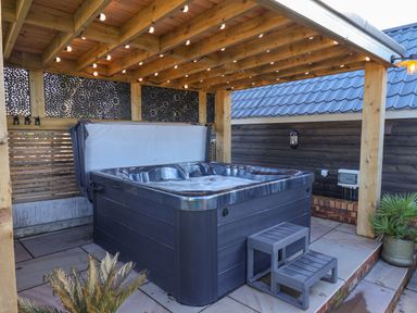 An outdoor hot tub under a wooden pergola with string lights and decorative panels at Foxes Den in Seamer North Yorkshire