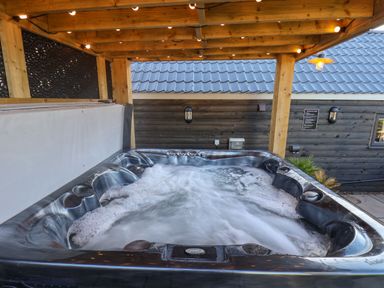 A bubbling hot tub under a wooden pergola next to a building with dark wood siding and a tiled roof at Foxes Den in Seamer North Yorkshire
