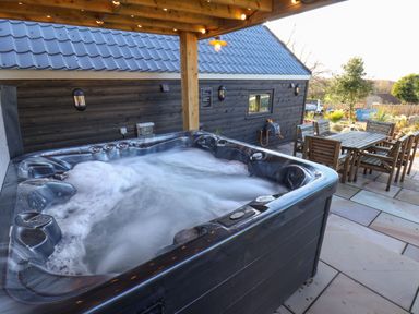 An outdoor hot tub with bubbling water on a patio next to a wooden dining table and chairs at Foxes Den in Seamer North Yorkshire