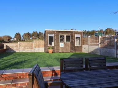 A backyard with a wooden shed a patio table and chairs and a grass lawn at Foxes Den in Seamer North Yorkshire