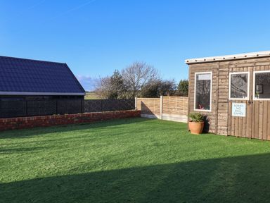 A garden with artificial grass a wooden shed with a no ball games sign and a potted plant at Foxes Den in Seamer North Yorkshire